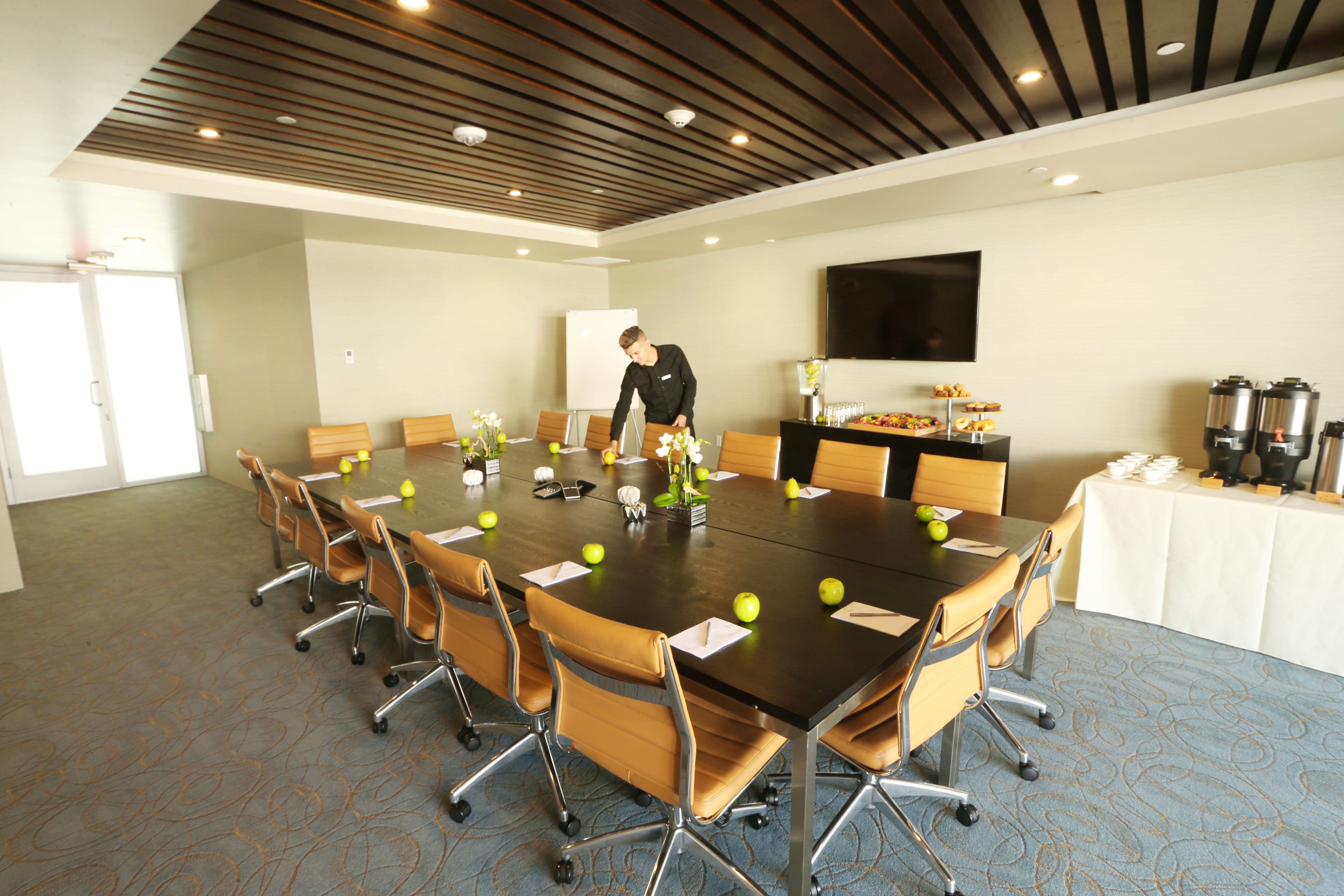 Une salle de conférence avec une longue table, des chaises, un tableau blanc et un téléviseur fixé au mur.