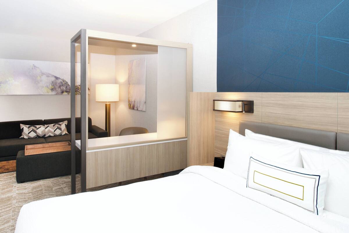 A modern hotel room with a large bed, a desk, a sofa, and a large mirror.