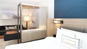 A modern hotel room with a large bed, a desk, a sofa, and a large mirror.