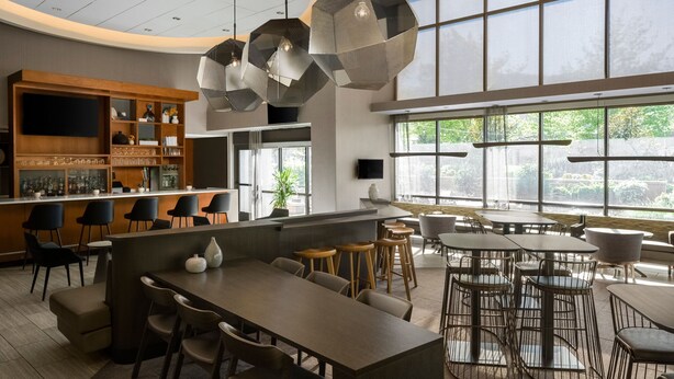 Un espace bar moderne doté d’un long comptoir, de nombreux sièges et de grandes fenêtres laissant entrer la lumière naturelle.