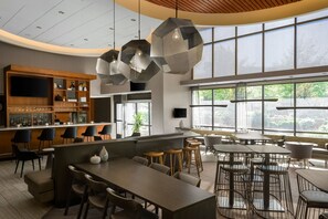 A modern bar area with a long counter, multiple seating options, and large windows providing natural light. - SpringHill Suites by Marriott Seattle Issaquah (Issaquah)