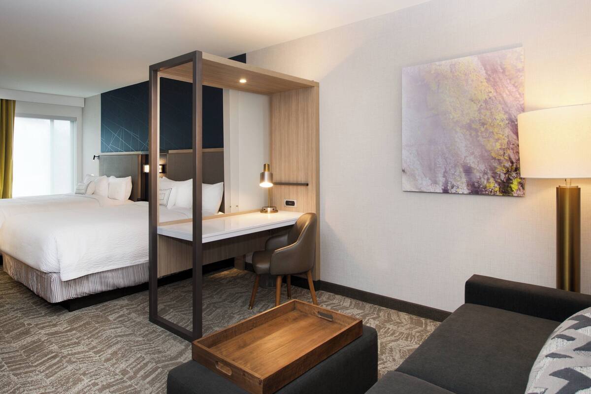 A hotel room with a bed, a desk, a chair, a sofa, and a wooden tray.