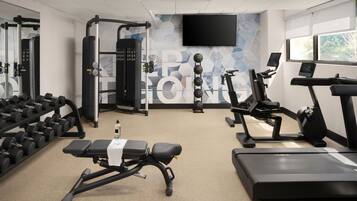 Een sportschool met trainingsapparatuur, een bank, gewichten, loopbanden en een televisie aan de muur.