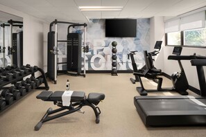A gym with exercise equipment, a bench, dumbbells, treadmills, and a TV on the wall. - SpringHill Suites by Marriott Seattle Issaquah (Issaquah)