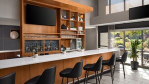 Un espace bar moderne doté d’un long comptoir, de plusieurs étagères où sont rangés les verres, et d’un téléviseur à écran plat fixé au mur.