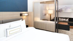 Une chambre d’hôtel avec un lit, une table de chevet, une lampe, un canapé et un grand miroir.