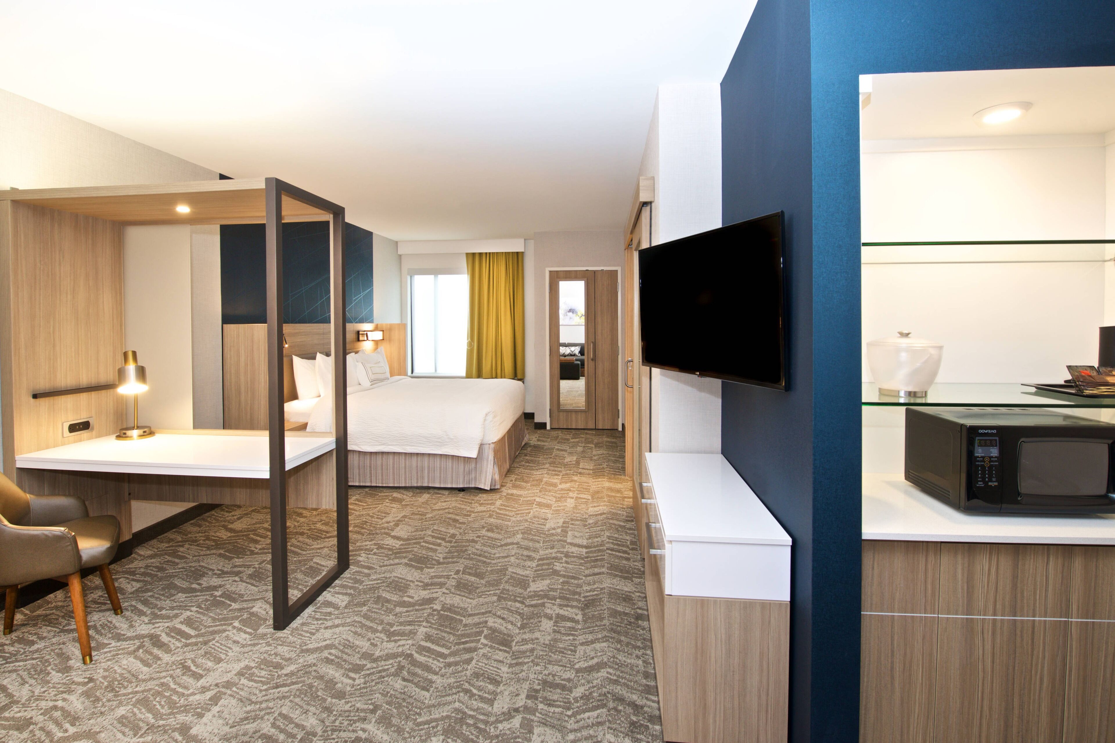 A hotel room with a bed, desk, chair, TV, and microwave.