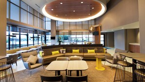 Un espace de détente moderne doté d’un grand coin salon, de plusieurs tables et offrant une vue dégagée grâce à de larges fenêtres.
