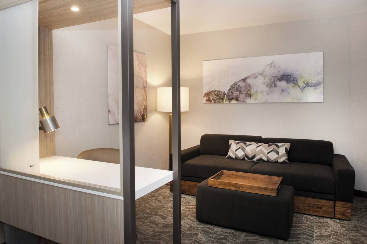 A modern hotel room with a sofa, ottoman, and a painting on the wall.