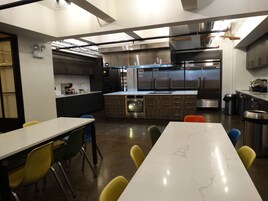 Una cocina moderna con electrodomésticos de acero inoxidable, encimera de mármol y una zona de estar con sillas amarillas.