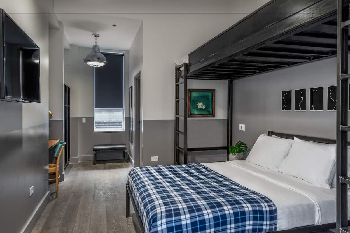 A modern hotel room with a bed, a bench, a desk, and a window.