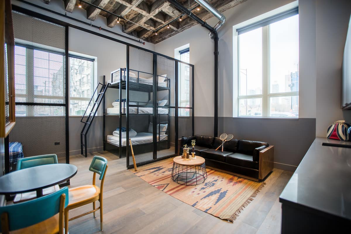 A modern room with bunk beds, a sofa, a round coffee table, and a view of the city through large windows.