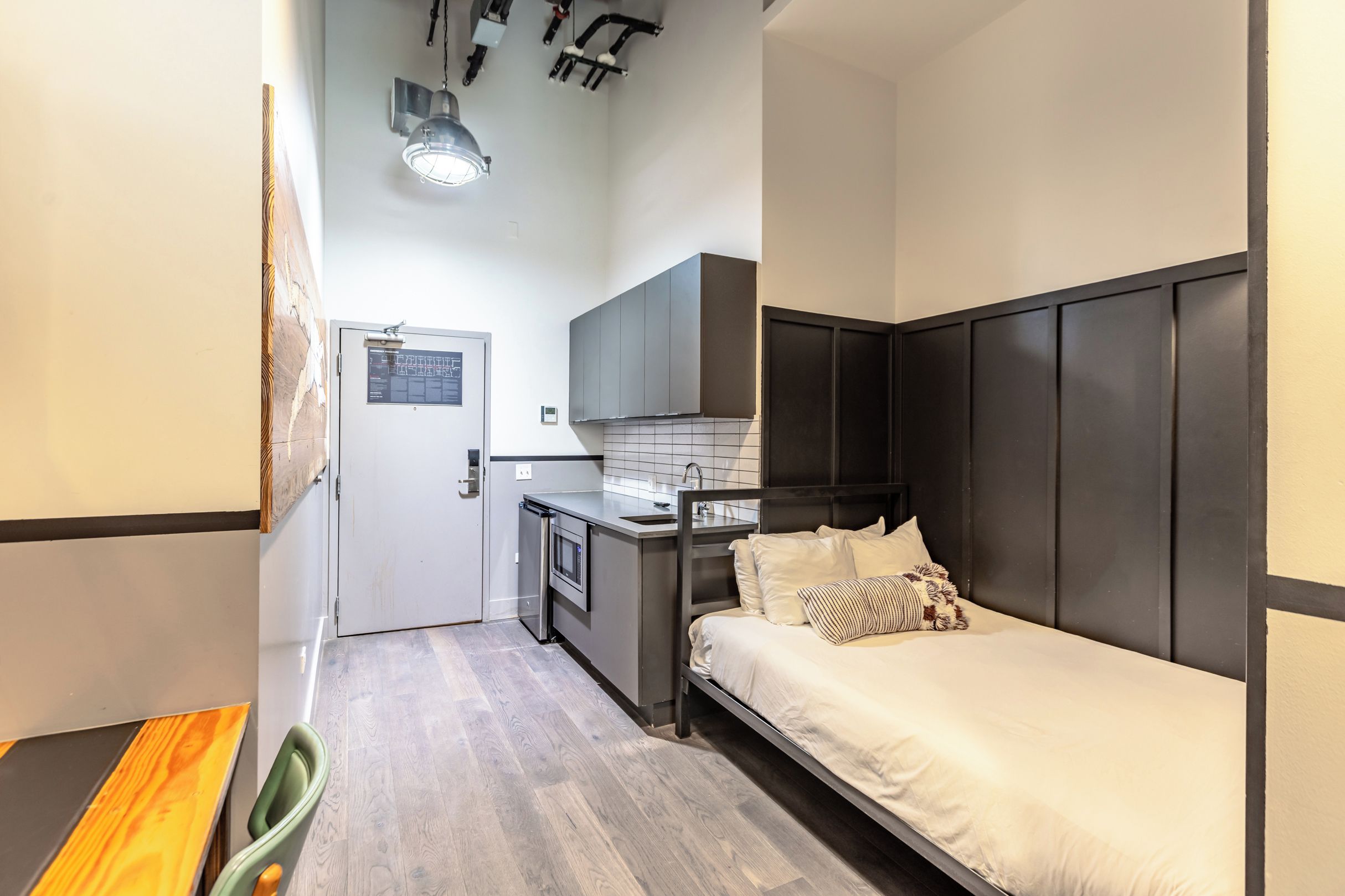 A compact room with a kitchenette, a bed with a headboard, and a small dining area.