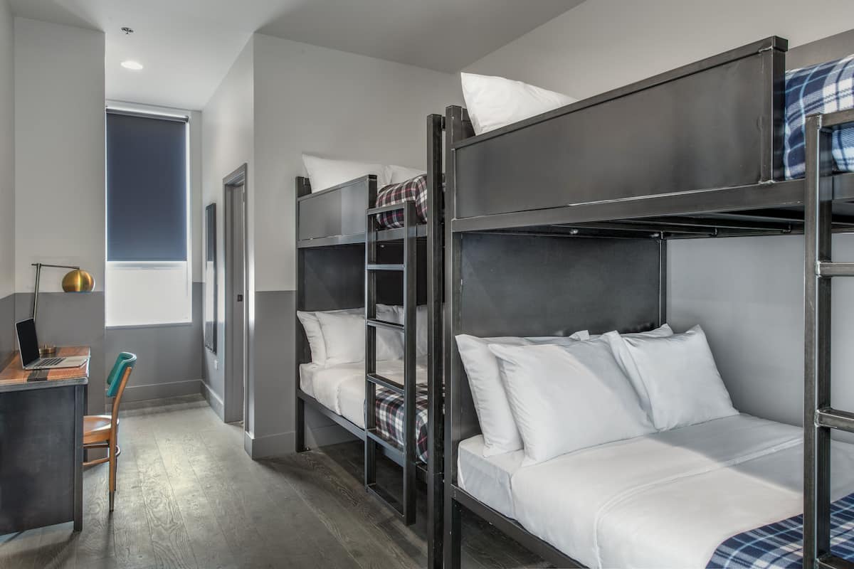 A bunk bed room with a desk and chair, a window, and a door.