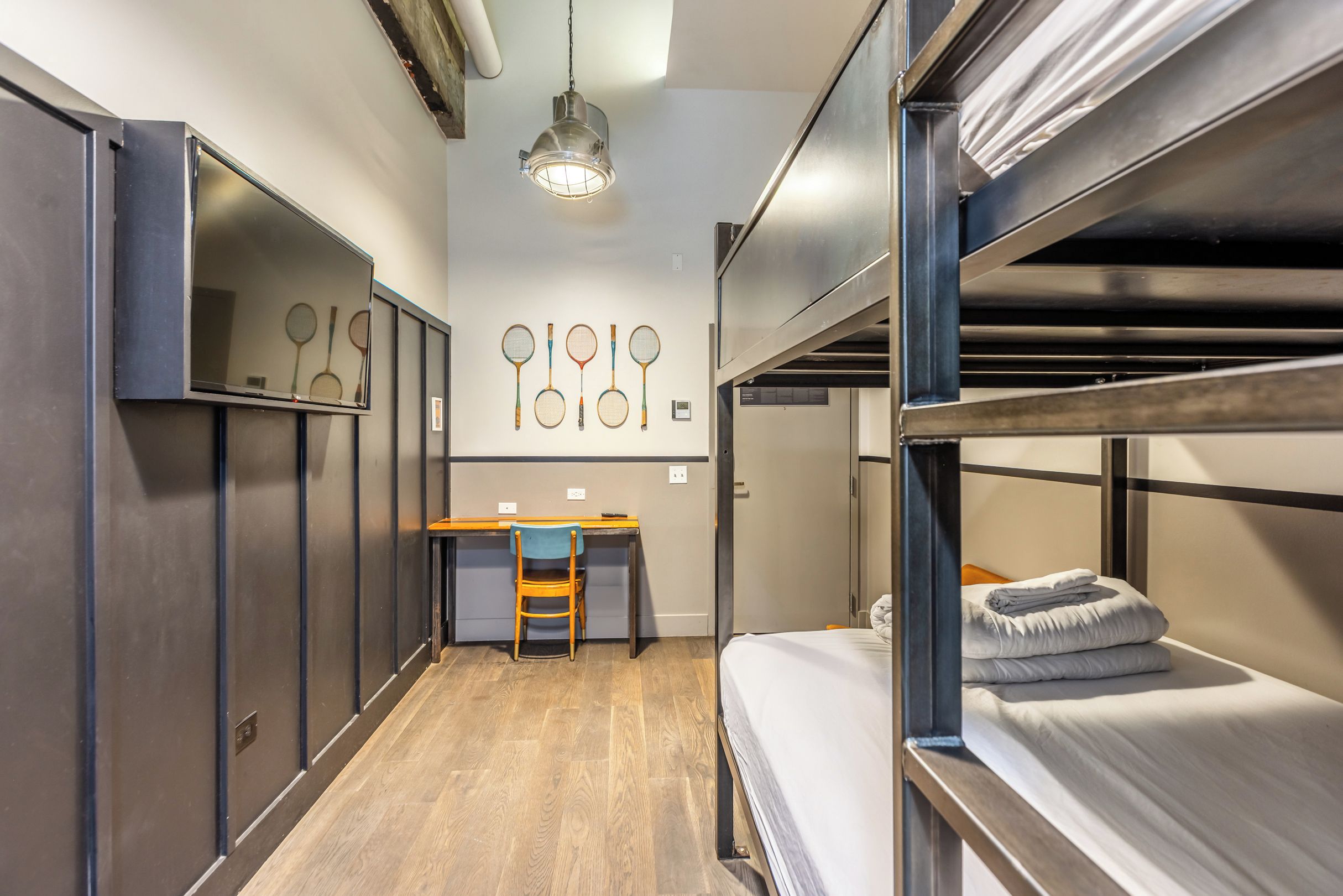 Une chambre avec un lit superposé, un bureau et des chaises, un luminaire suspendu et un mur décoré de raquettes de tennis.