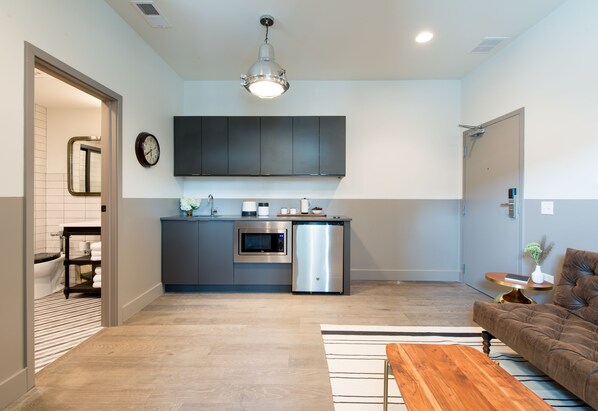 A modern kitchen with grey cabinets, a microwave, and a dishwasher. There is a wooden coffee table and a brown sofa in the living area. - The Chicago Hotel Collection River North (Chicago)