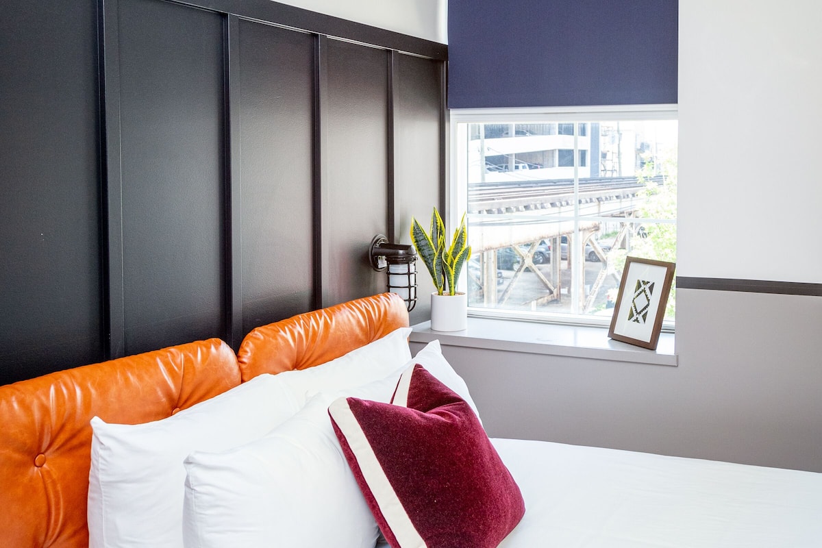 A hotel room with a bed, a window with a view, a plant, and a framed picture on the windowsill.