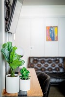 Una habitación con una mesa de madera, dos plantas en macetas, un sofá y un cuadro en la pared.