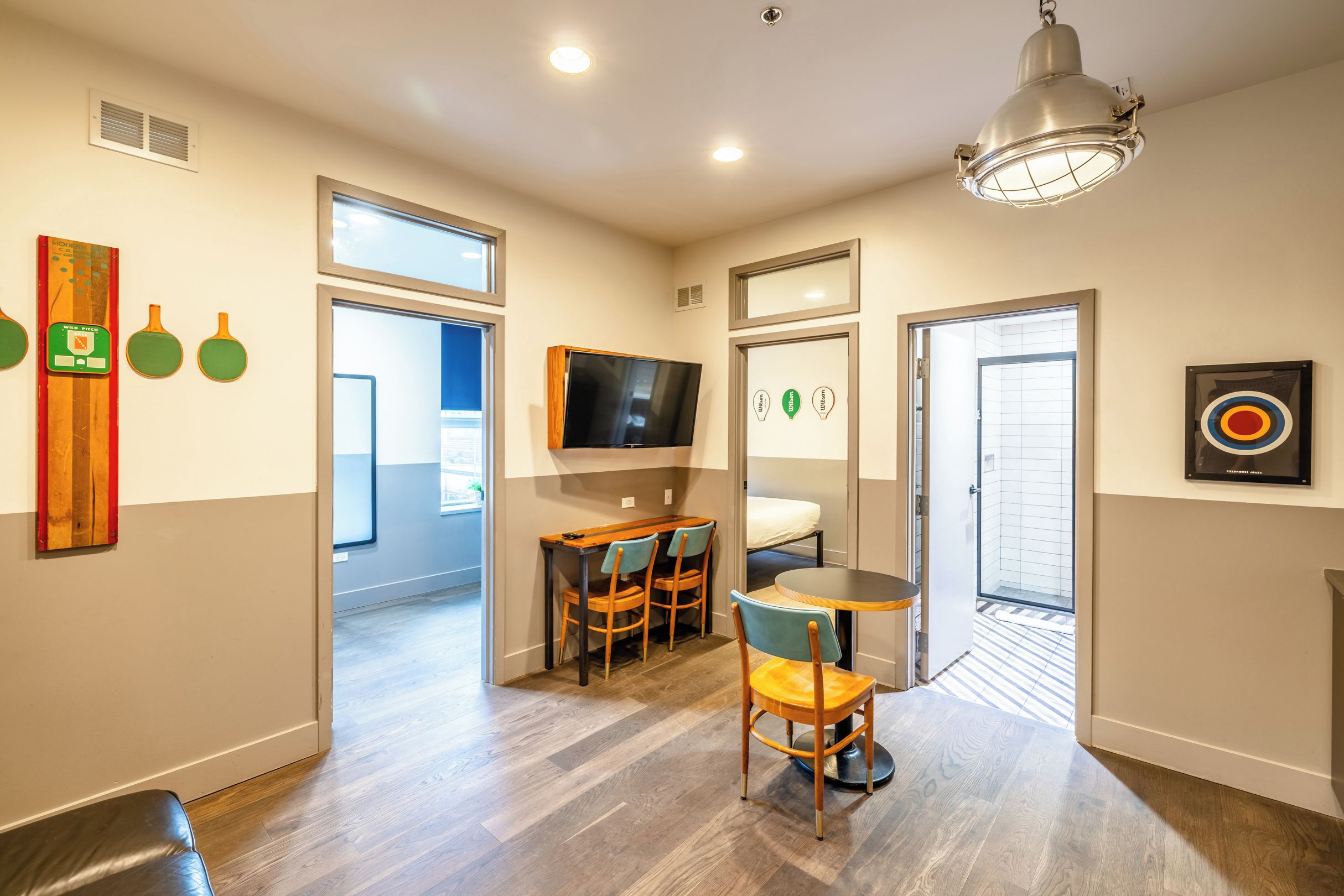Habitación de hotel con piso de madera, comedor con mesa y sillas, televisor y ducha.
