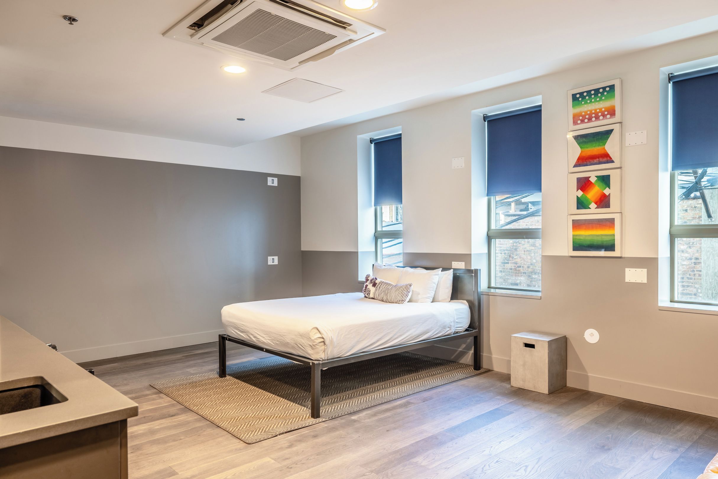 Une chambre à coucher moderne, avec un lit, une petite table de chevet, une fenêtre donnant sur un beau paysage et un mur décoré d’œuvres d’art.