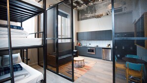 Moderni hotellihuone, jossa on kerrossängyt, keittotila ja oleskelualue pyöreän pöydän kera.