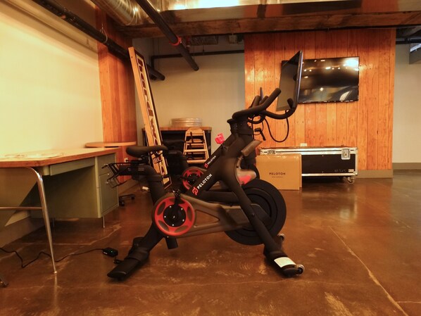 A stationary bike in a room with wooden walls, a desk, and a television mounted on the wall. - The Chicago Hotel Collection River North (Chicago)
