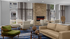 A modern living room with a stone fireplace, comfortable seating, and a view through large windows. - Fairfield Inn & Suites Savannah Downtown/Historic District (Savannah)