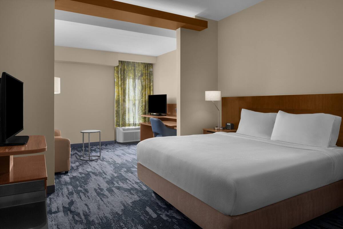 Una habitación de hotel con una cama grande, un escritorio con silla, televisión y ventana con cortinas.