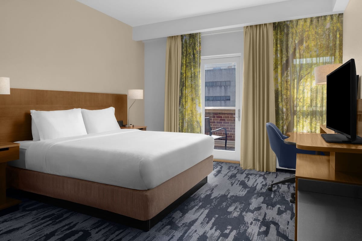 Una habitación de hotel con una cama grande, un escritorio con computadora, una silla y un televisor.