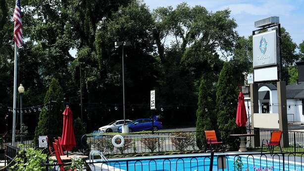 A swimming pool area with a fence, lounge chairs, and a flag. - Twi-Lite Inn (Front Royal)