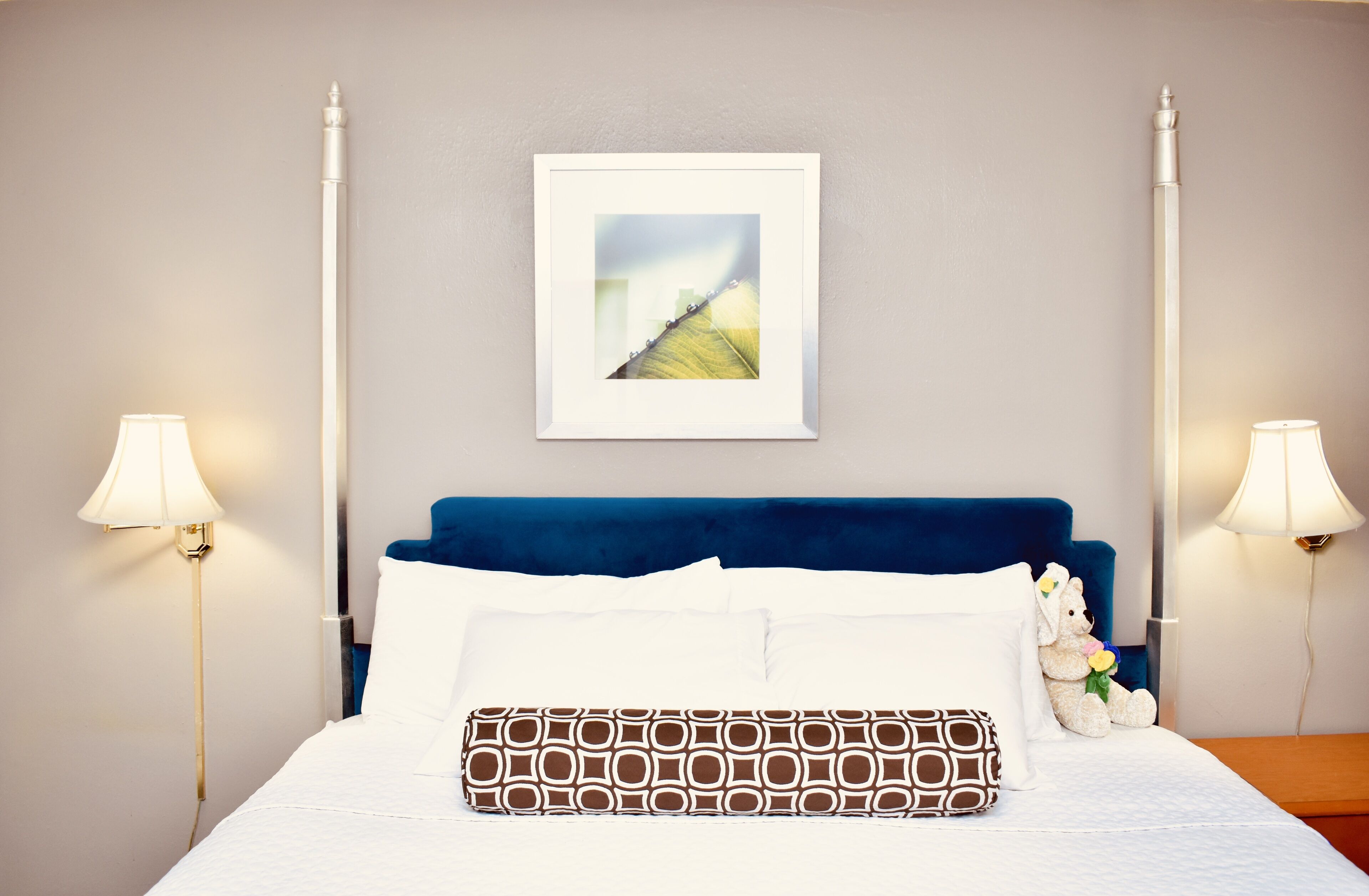A neatly made bed with white and patterned pillows, a blue headboard, and a framed picture above.