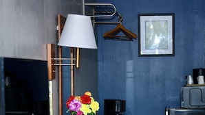 A compact hotel room with a small round table, a coffee maker, a vase with flowers, a lamp, a framed picture on the wall, and a refrigerator. - Twi-Lite Inn (Front Royal)