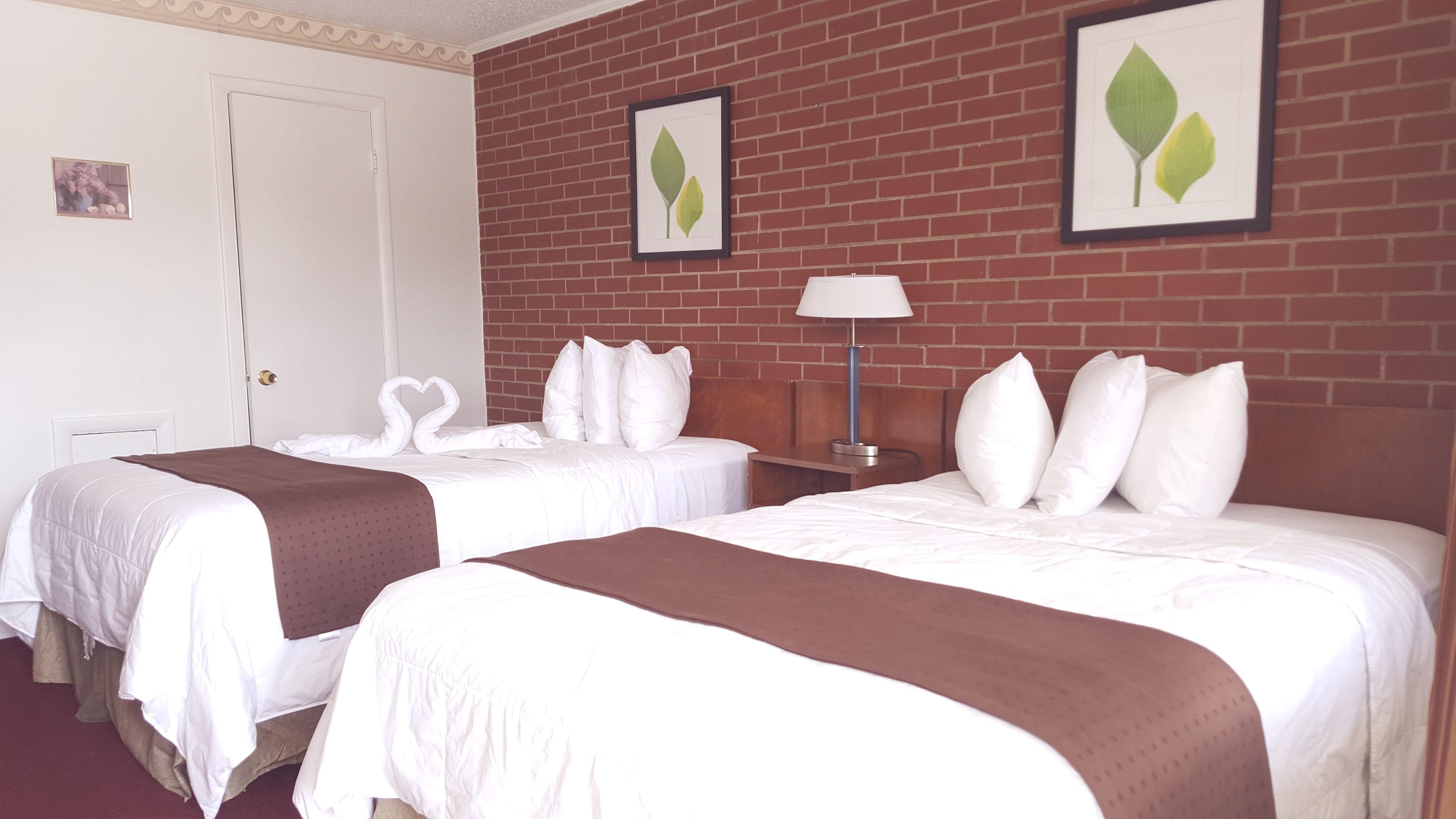 Habitación de hotel con dos camas, una pared de ladrillo y obras de arte con hojas enmarcadas.