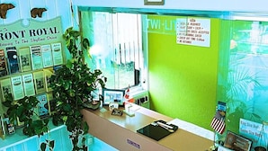 A reception desk with a green wall, a plant, and various informational posters. - Twi-Lite Inn (Front Royal)