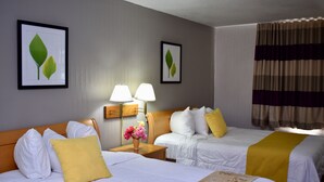 A hotel room with two beds, a nightstand with lamps, a vase with flowers, and framed leaf artwork on the walls. - Twi-Lite Inn (Front Royal)