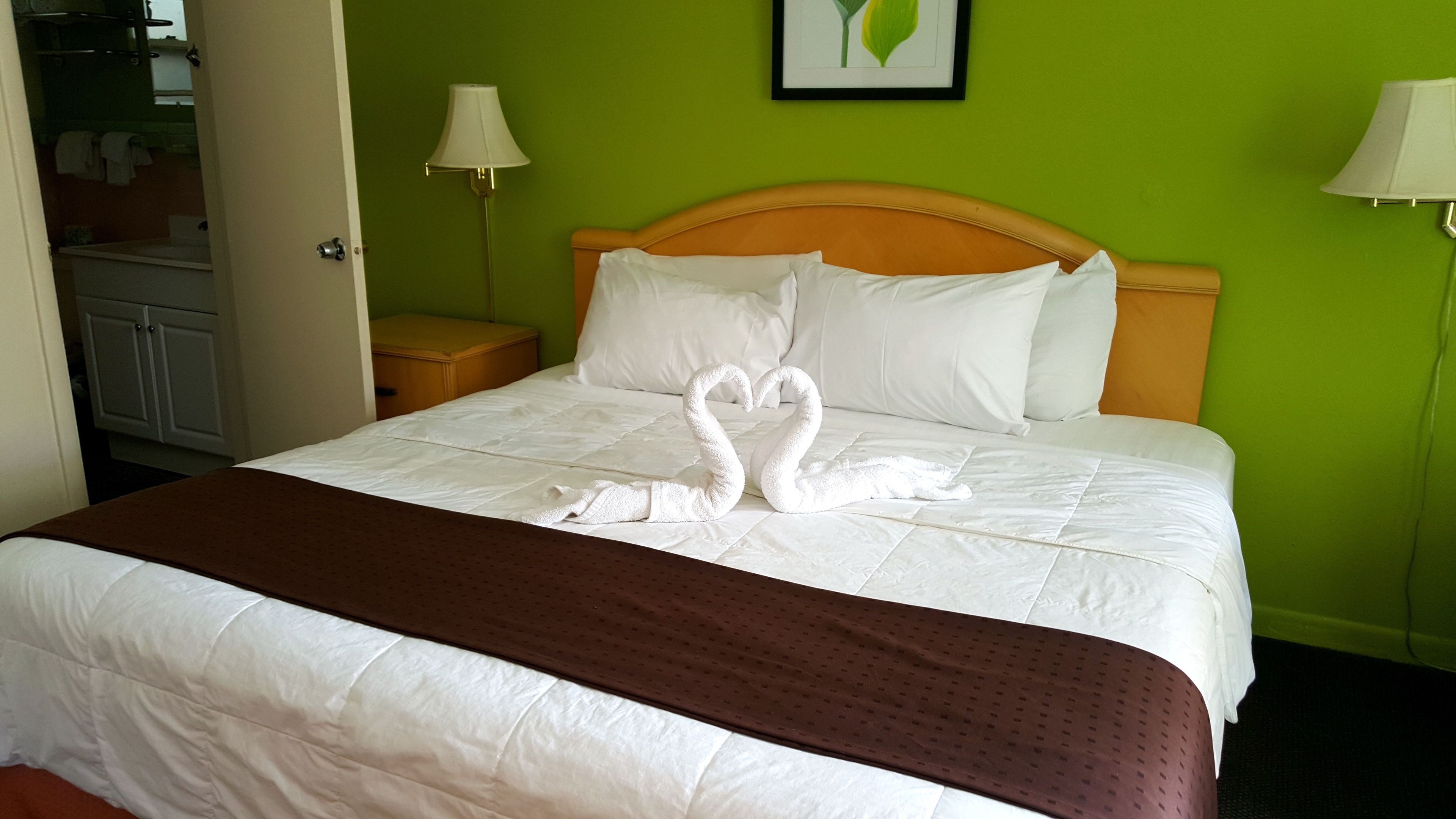 A hotel room with a bed, green walls, and a framed artwork on the wall.