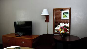 A hotel room with a TV on a wooden dresser, a lamp, a mirror with a picture, and a small table with a vase of flowers.