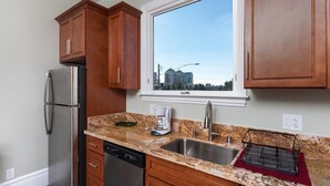A kitchen with wooden cabinets, a stainless steel refrigerator, a granite countertop, a coffee maker, and a window with a city view. - Stunning 1 Bedroom Flat (Oakland)