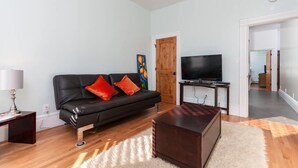 A living room with a black leather sofa, a flat-screen TV on a stand, a wooden coffee table, and a fluffy rug. - Stunning 1 Bedroom Flat (Oakland)