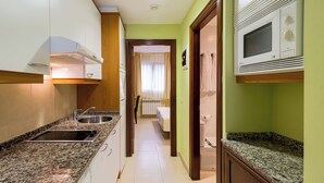 Une cuisine compacte équipée d’un four à micro-ondes encastré, d’un évier et d’une cuisinière. Une porte en bois donne accès à une salle de bain avec des toilettes et une douche.