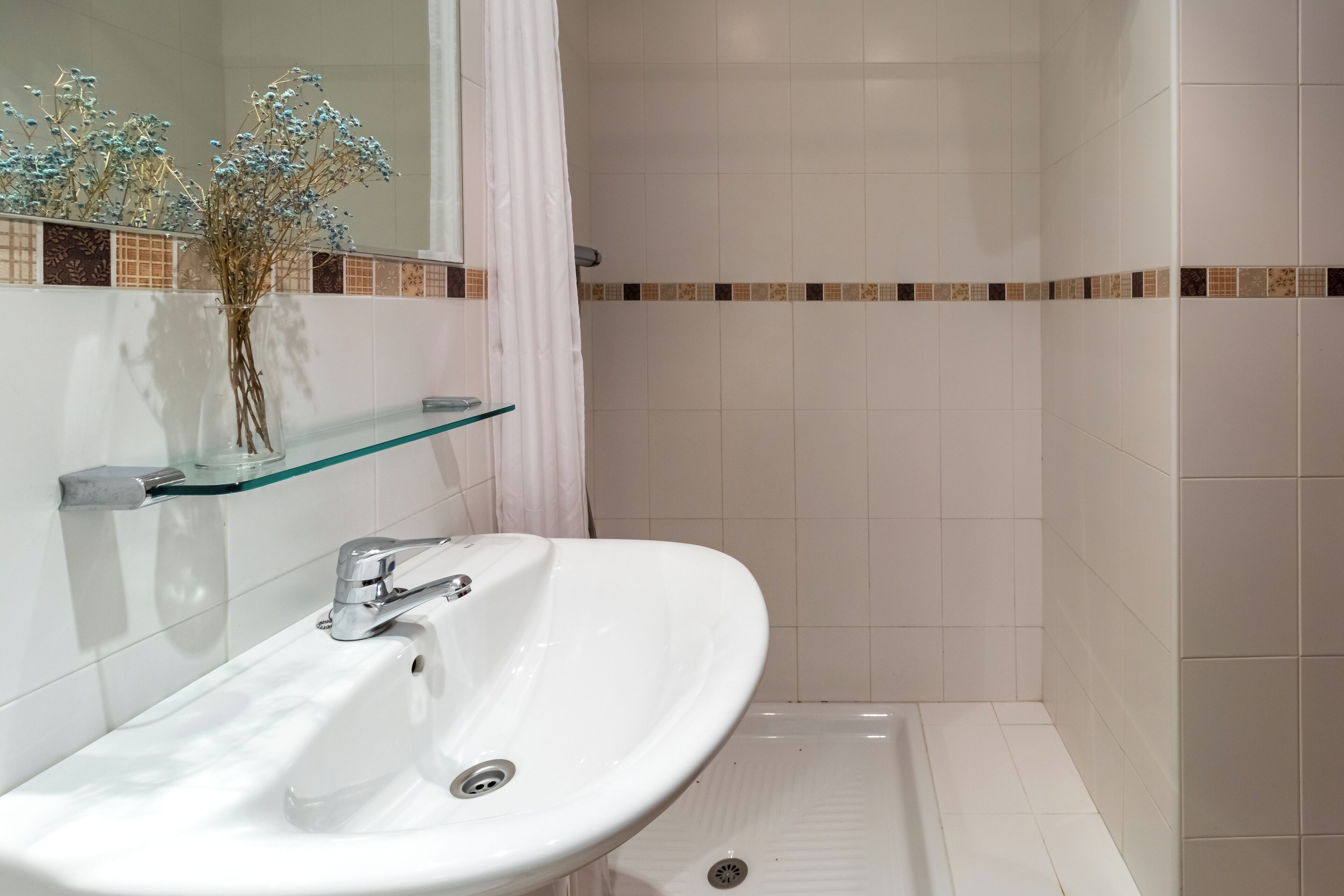 A bathroom with a white sink, a glass shelf, and a shower area.