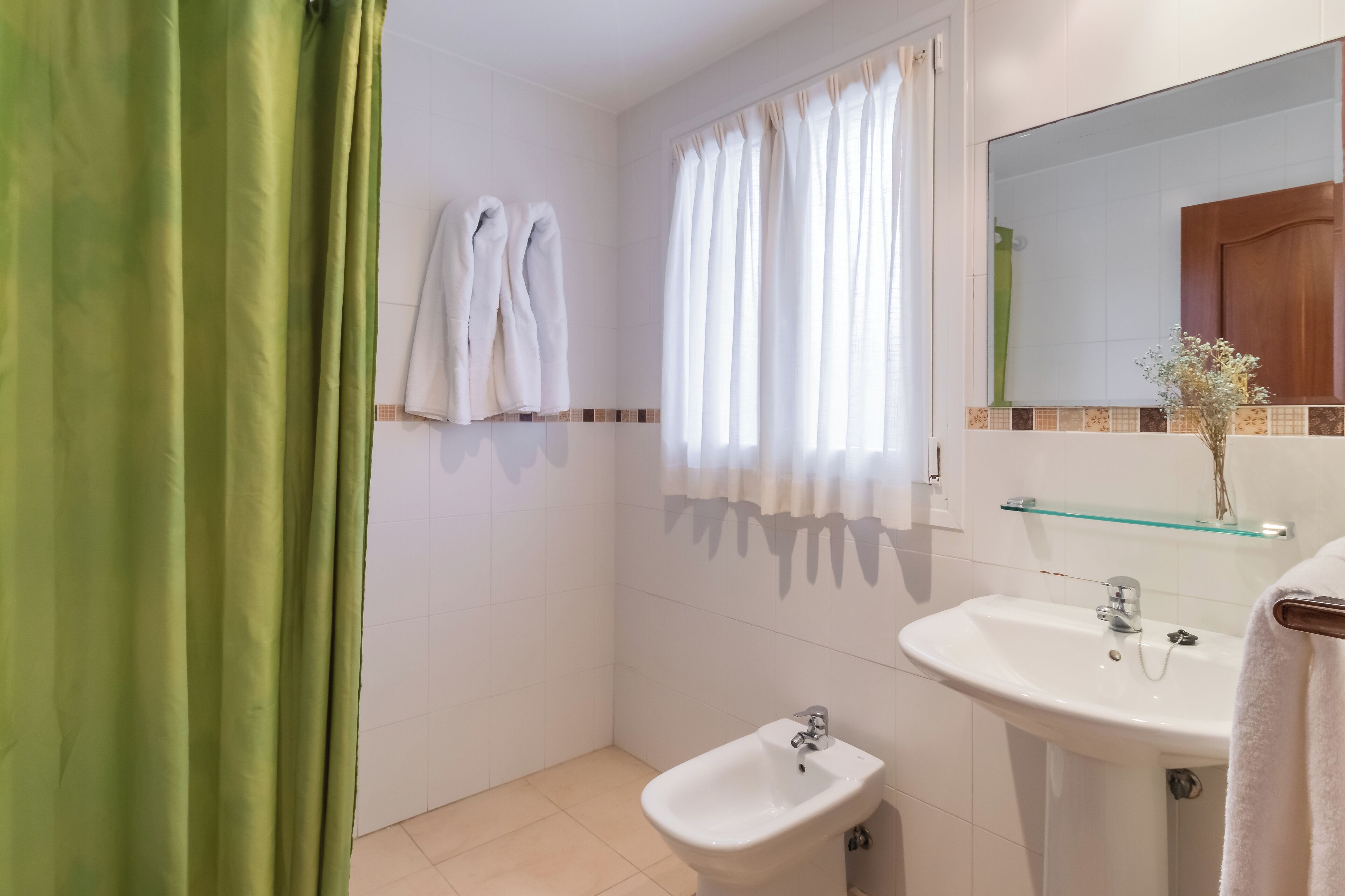 Ein Badezimmer mit grünem Duschvorhang, weißen Handtüchern, einem Bidet, einem Waschbecken und einem Spiegel mit Ablagefläche.