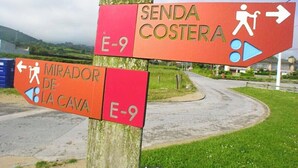 Un panneau indicateur directionnel, doté de plusieurs flèches et symboles, indique les directions à suivre pour se rendre à « Senda Costerá » et au « Mirador de La Cava », le long de la route E-9.