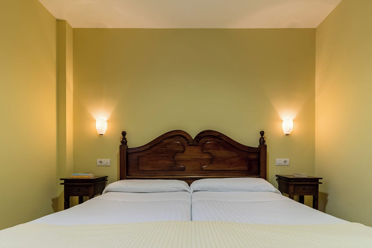 Un lit double avec une tête de lit en bois, deux tables de chevet et des lampes fixées au mur.