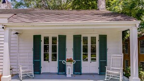 A white building with green shutters, a covered porch, and two rocking chairs. - Steele Cottage (Vicksburg)