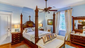A four-poster bed with a ceiling fan, a wooden dresser, and a window with curtains. - Steele Cottage (Vicksburg)