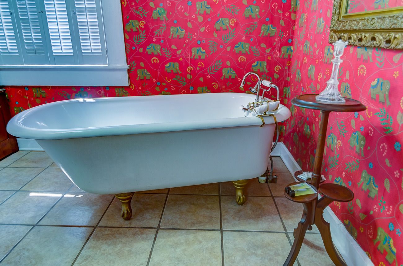 Un baño con una bañera independiente, una pequeña mesa redonda con una vela y papel tapiz estampado.
