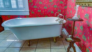 Un baño con una bañera independiente, una pequeña mesa redonda con una vela y papel tapiz estampado.