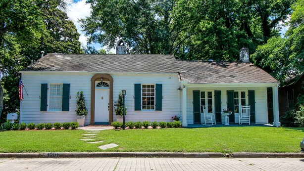 A white house with green shutters, a front porch, and a small garden. - Steele Cottage (Vicksburg)