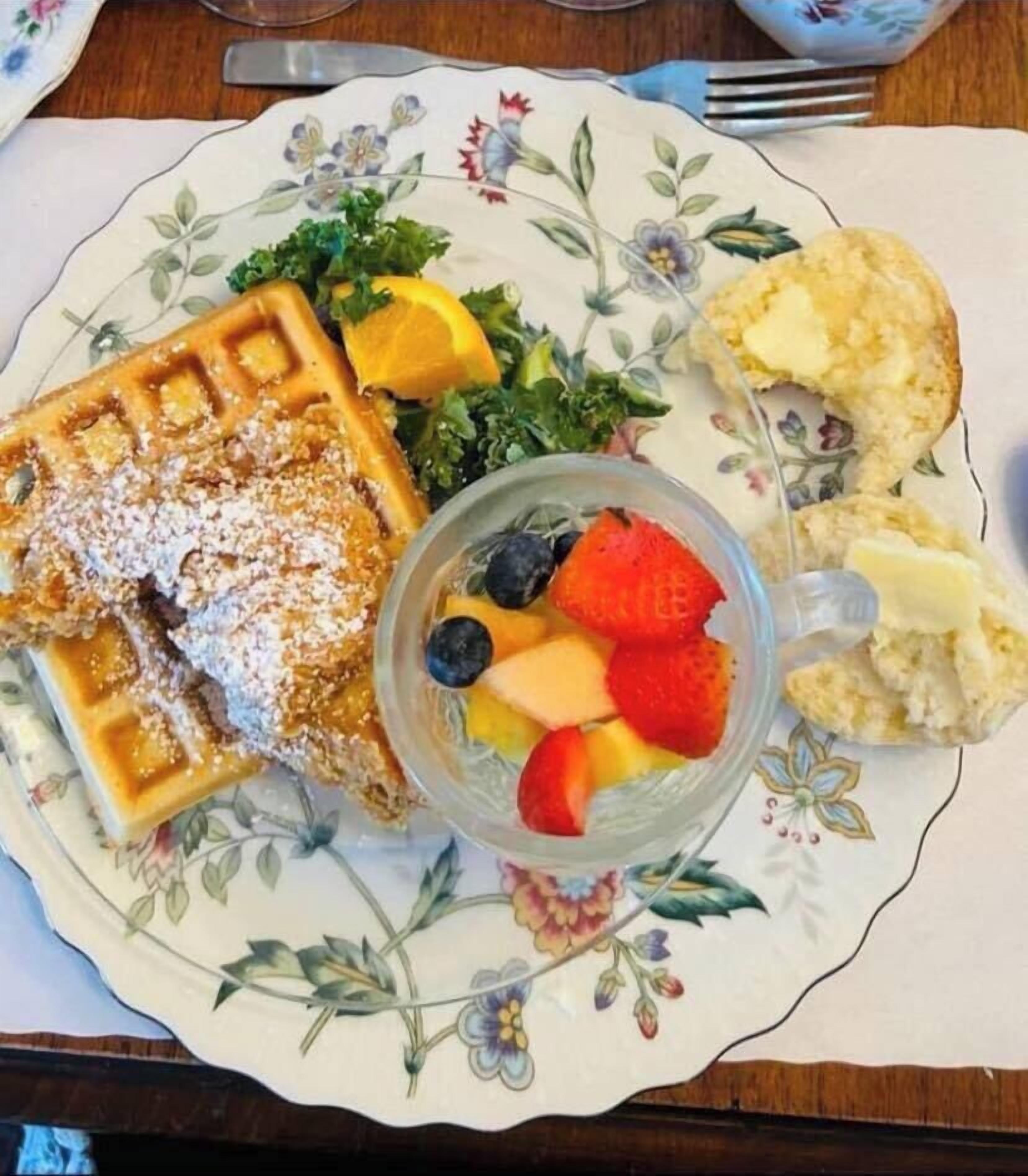 Une assiette contenant des gaufres, des fruits et du beurre, posée sur une nappe à motifs floraux.